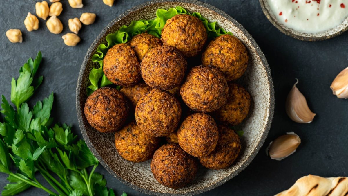 Eine Schale Falafel mit Erdnüssen in der Draufsicht, daneben eine Schüssel Joghurt, Kräuter und Kichererbsen.