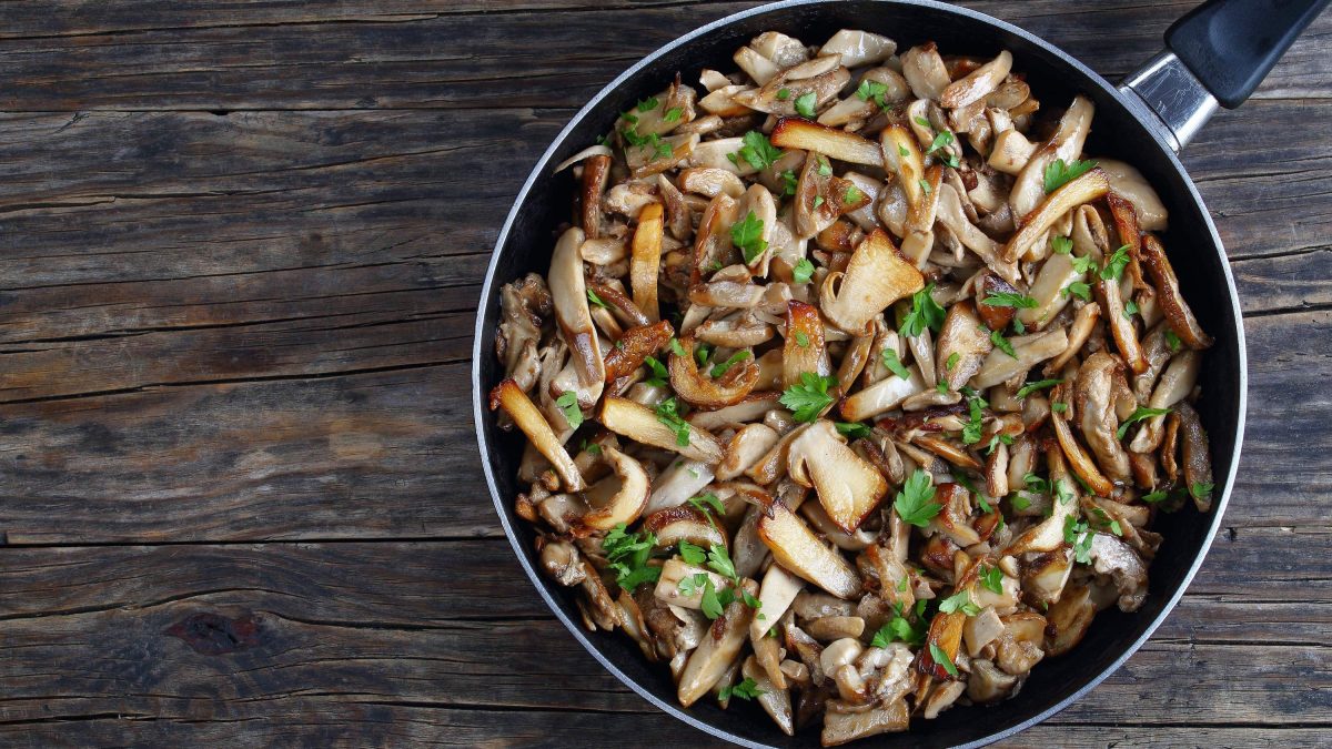 Eine Pfanne mit italienischer Antipasti: Funghi Trifolati mit Petersilie und Knoblauch in einer großen Pfanne auf hölzernem Untergrund, von oben fotografiert.