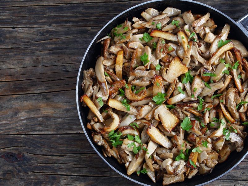 Eine Pfanne mit italienischer Antipasti: Funghi Trifolati mit Petersilie und Knoblauch in einer großen Pfanne auf hölzernem Untergrund, von oben fotografiert.