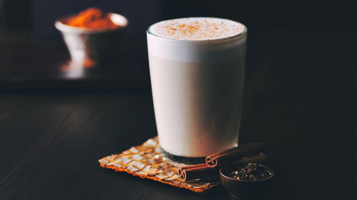 Ein Glas Goguma Latte mit Milchschaum und Zimt bestreut auf dunklem Untergrund.