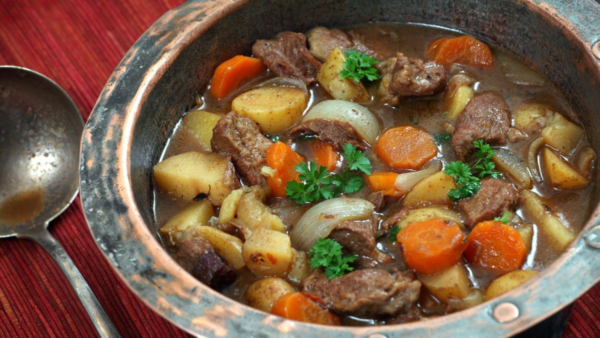 St. Patrick's Day Irish Stew in traditionellem Teller aus Steingut auf Holztisch. Daneben antiker Silberlöffel. Draufsicht.