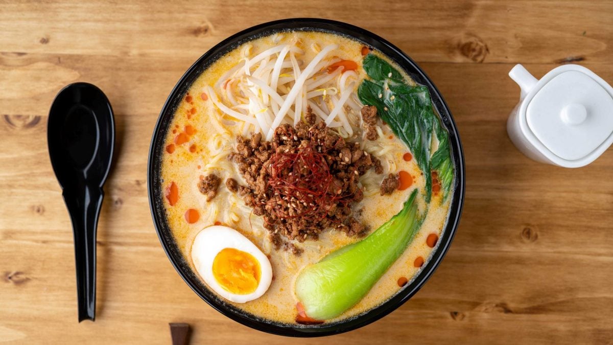 Japanische Nudelsuppe mit Ei, Hackfleisch, Nudeln, Pak Choi und Sojasprossen in einer Schüssel mit Löffel.