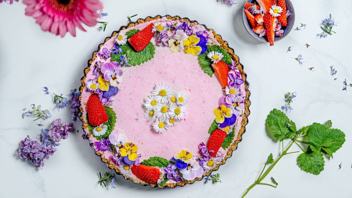 Aus der Vogelperspektiv: Auf einem hellblauen Untergrund steht Kuchen mit Erdbeeren und ganz vielen kandierten Blüten.