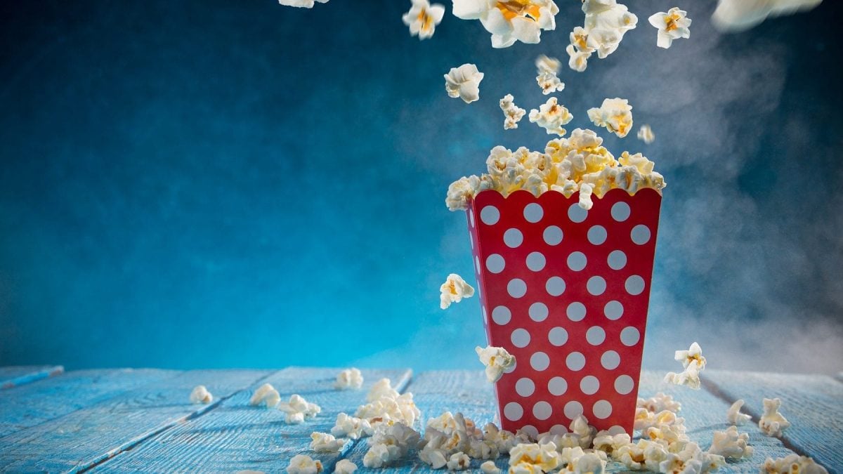 vor einem blauen hintergrund ist eine rote weiße gepunktete popcorntuete zu sehen. aus der springen popcornkoerner. das foto bebildert das buch Kochen in Perfektion : Profi-Wissen für die Kueche