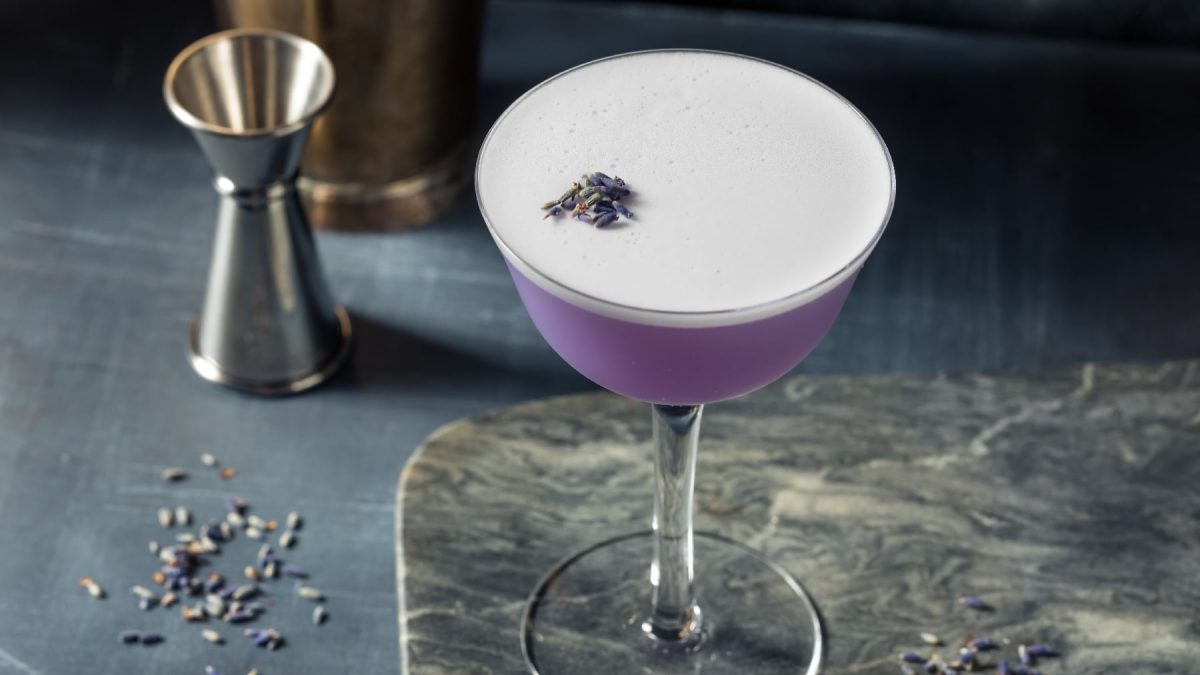 Gin Glas mit lila Flüssigkeit auf einem grauen Untergrund.