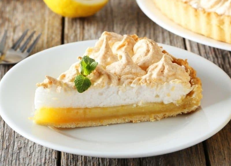 Limoncello-Tarte mit Baiserhaube auf einem weißen Teller. Das Ganze auf einem hölzernen Untergrund.