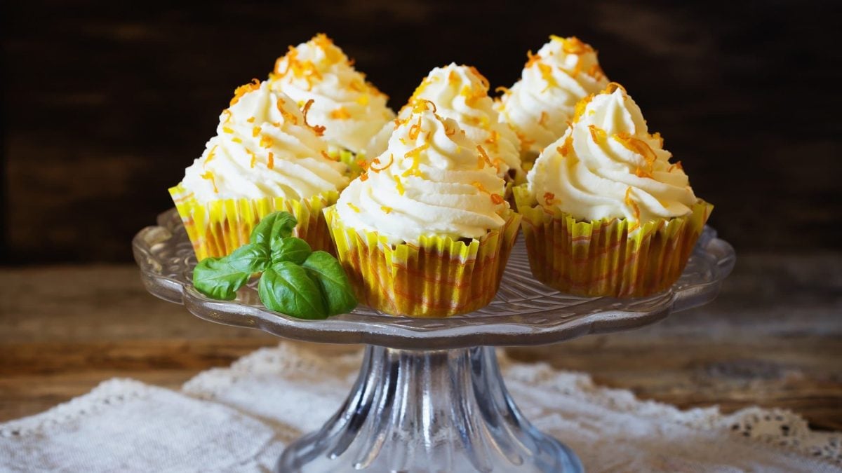 Ein Tortenständer, auf dem sechs Möhren-Cupcakes mit Orange stehen.