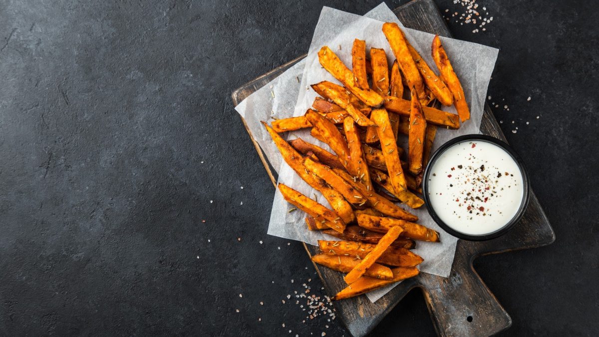 Möhren Pommes mit Sour Cream. Das Ganze auf einem dunklen Holzbrett auf einem dunklen Untergrund.