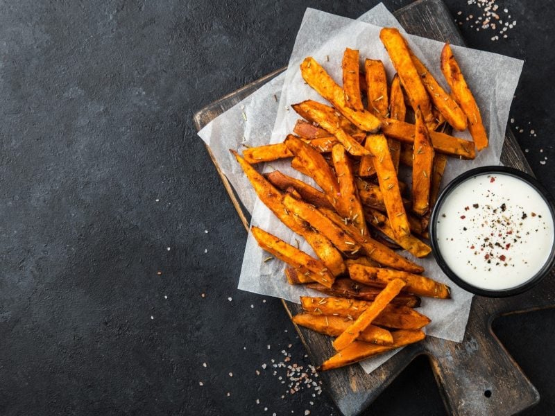 Möhren Pommes mit Sour Cream. Das Ganze auf einem dunklen Holzbrett auf einem dunklen Untergrund.