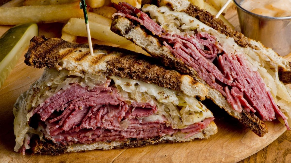 Angeschnittenes Reuben Sandwich von der Seite mit Pommes im Hintergrund auf Holztisch