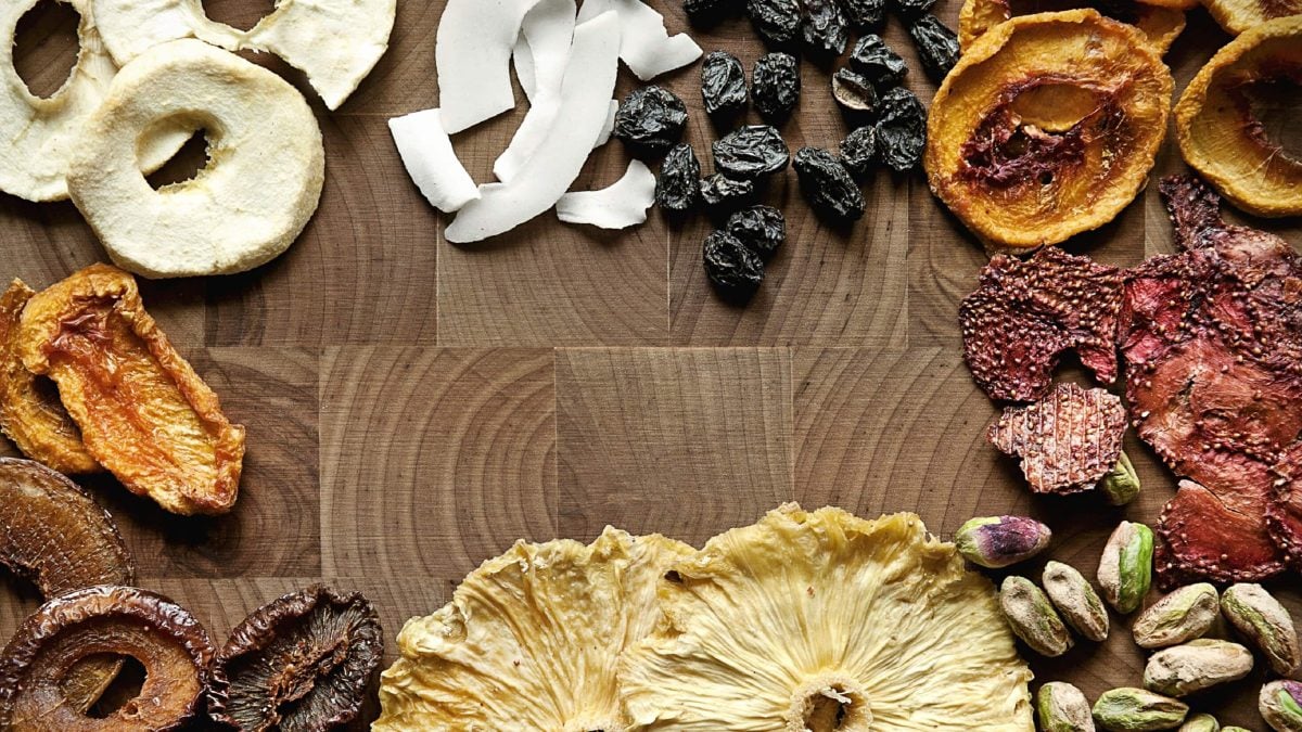 Eine Vielzahl an selbst gemachten Trockenfrüchten auf einem Tisch verteilt, unter Anderem Nüsse, Pilue, Aprikosen, Äpfel, Kokosnuss, Rosinen und Aprikosen.
