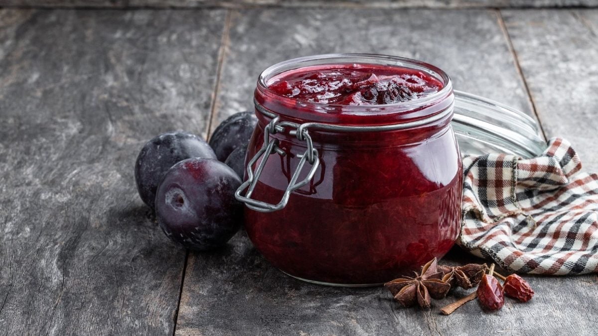 Selbst gemachtes Pflaumen-Chutney mit Nelken und Sternanis, in einem Marmeladenglas, serviert auf einem hölzernen, grauen Tisch.
