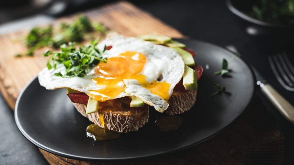 Schwarzer Teller in der Draufsicht mit Brot, Avocado, Sucuk und einem Spiegelei