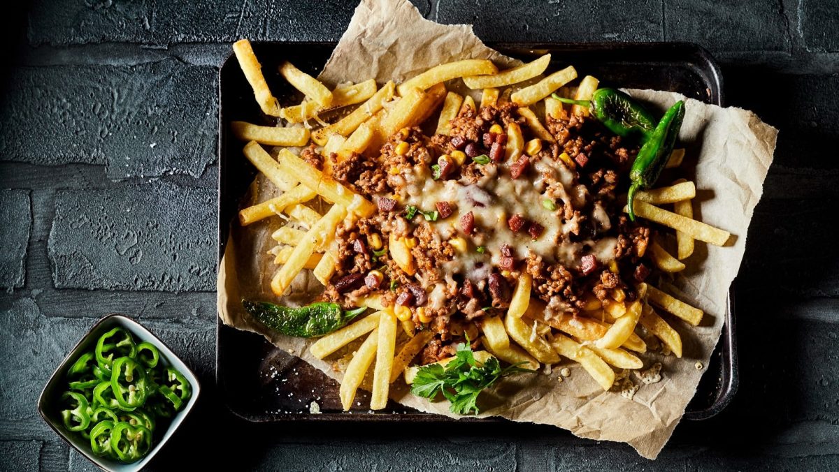 Ein Backblech vegane Chili Cheese Fries mit frischer Petersilie in der Draufsicht.