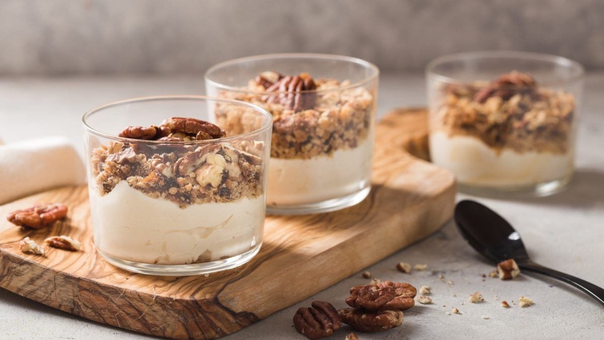 Drei Dessertgläser mit veganer Vanille-Mousse und Müsli auf einem Holzbrett.