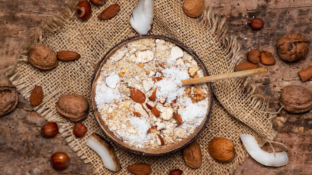 Würziger Nuss-Porridge mit frischem Ingwer, Kokosflocken und Gewürzen in einer Schale auf einem Tisch aus Holz