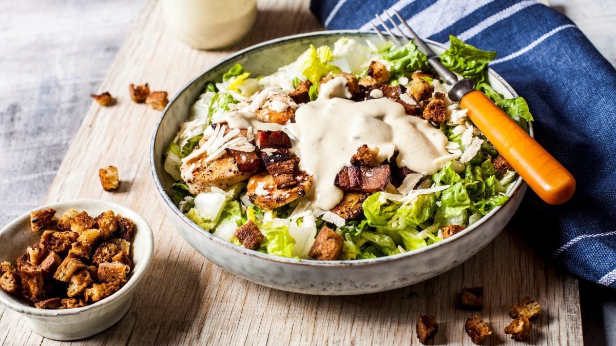 Schüssel mit Caesar Salat angerichtet auf einem Holzbrett.