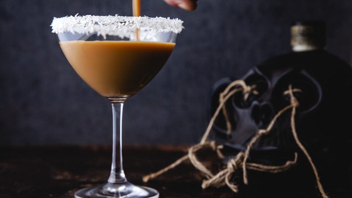 Auf einem Tisch steht ein Cocktail mit Eierlikör, Rum und Espresso. Der Rand des Glases ist mit Kokosraspeln verziert.