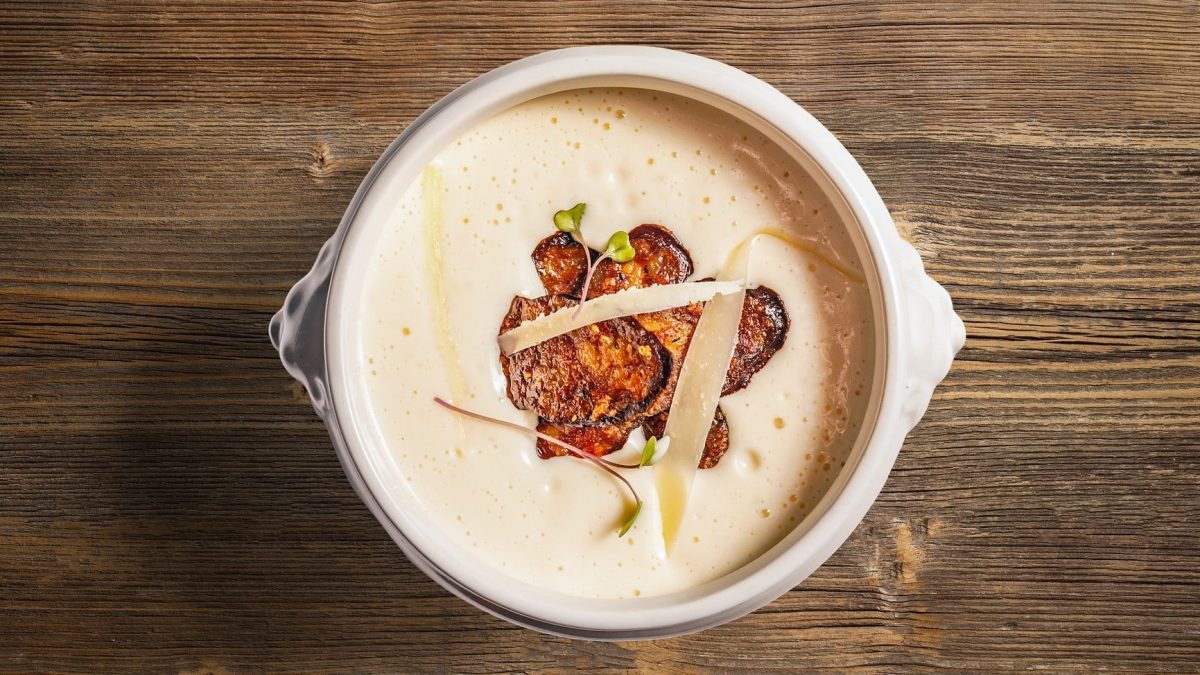Knoblauchcremesuppe mit gebratener Salami in weißer Schüssel, angerichtet auf Holzplatte.