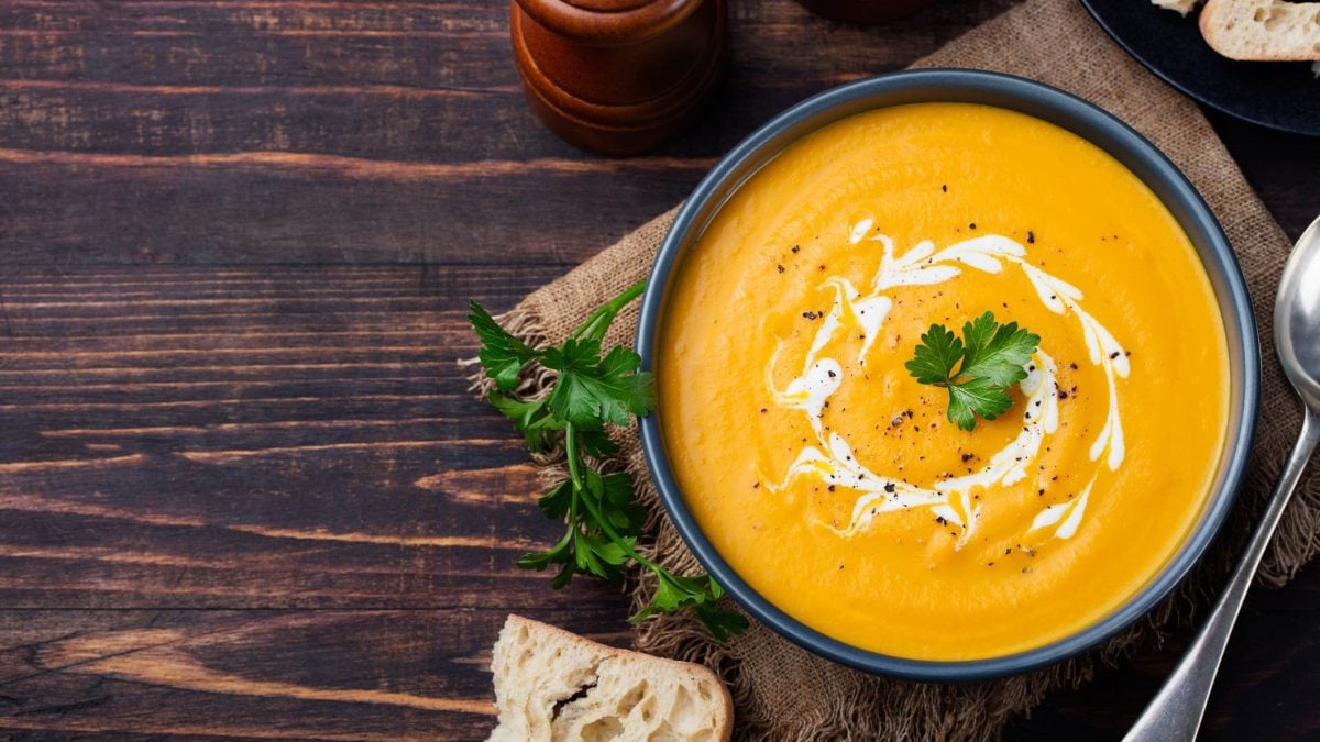 Dunkle Schüssel gefüllt mit Möhren-Ingwer-Suppe auf hölzernem Untergrund.