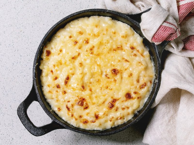 Schwarze gusseiserne Form gefüllt mit Käse-Makkaroni auf weißem Untergrund.