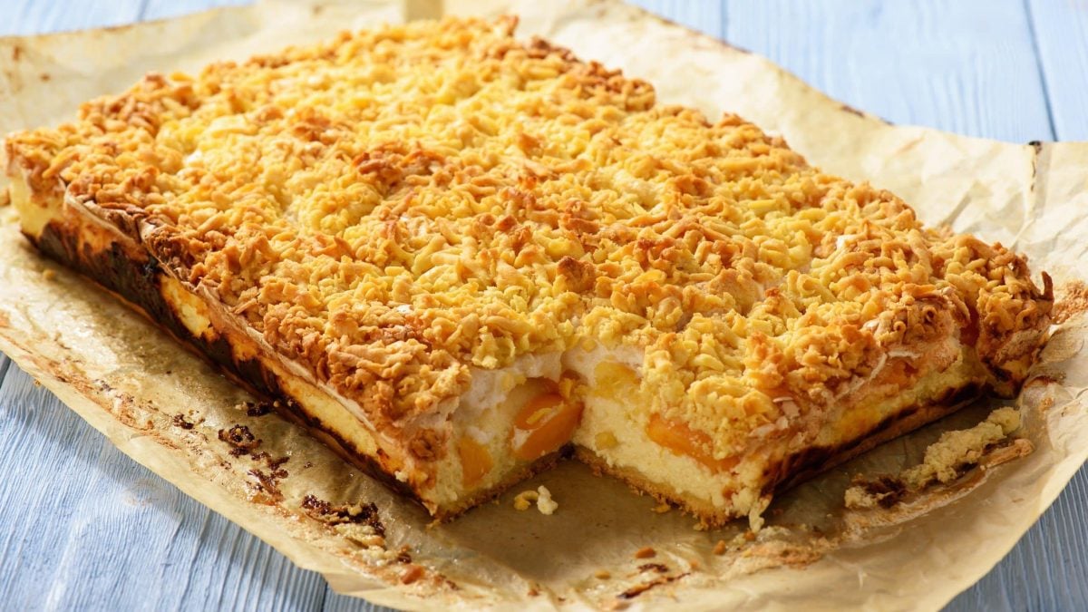 Pfirsich-Käsekuchen auf Backpapier auf hellblauem, hölzernem Untergrund.