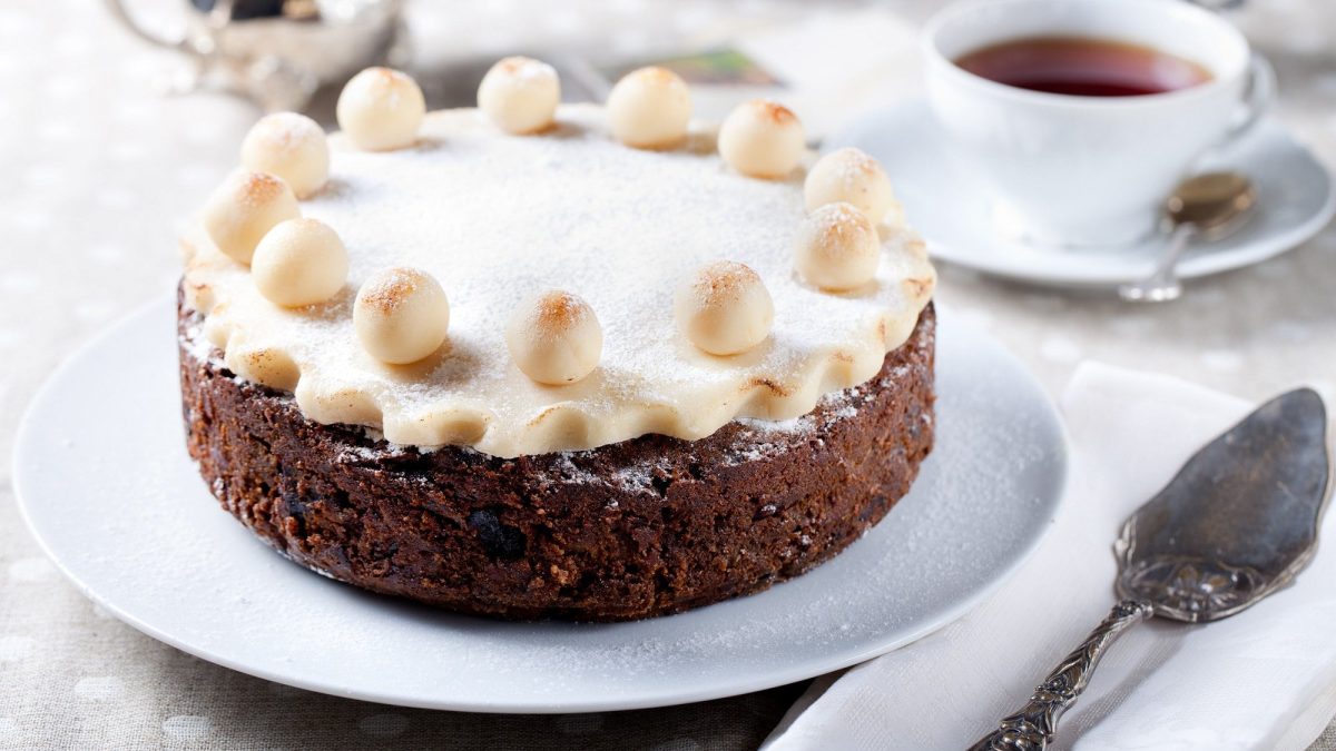 Simnel Cake auf einem weißen Teller. Daneben steht eine Tasse Tee.