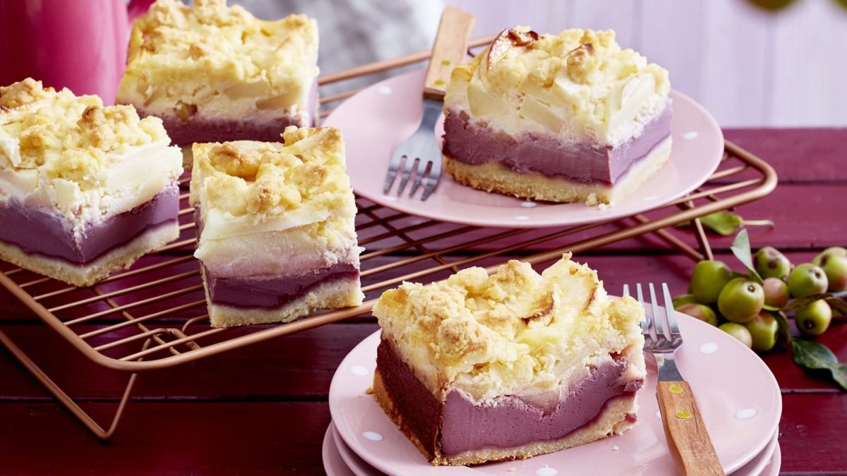 Apfelholunder-Streuselkuchen auf einem rosa Teller neben einer Gabel auf einem gedeckten Tisch