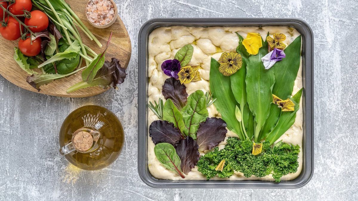 Eine Bärlauch-Focaccia vor dem Backen, ihr Belag ist als Blumenwiese belegt.
