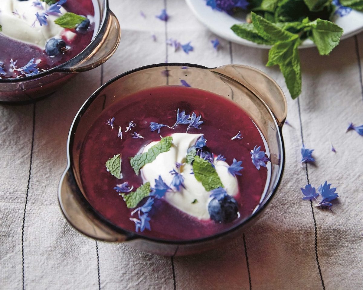 Zwei Glasschalen mit Heidelbeersuppe, Minze, Joghurt und Blüten auf einem Geschirrtuch, ein Rezept aus dem Kochbuch "Baltikum".