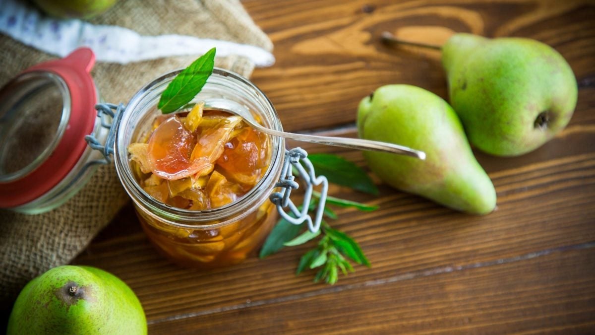 Birnen-Chutney geöffnet in einem Einweckglas, garniert mit Kräutern auf einem Holztisch, umgeben von ganzen frischen Birnen