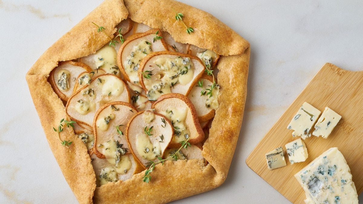 Birnen Galette mit Gorgonzola auf einem weißen Untergrund. Daneben ein Holzbrett mit Gorgonzola.