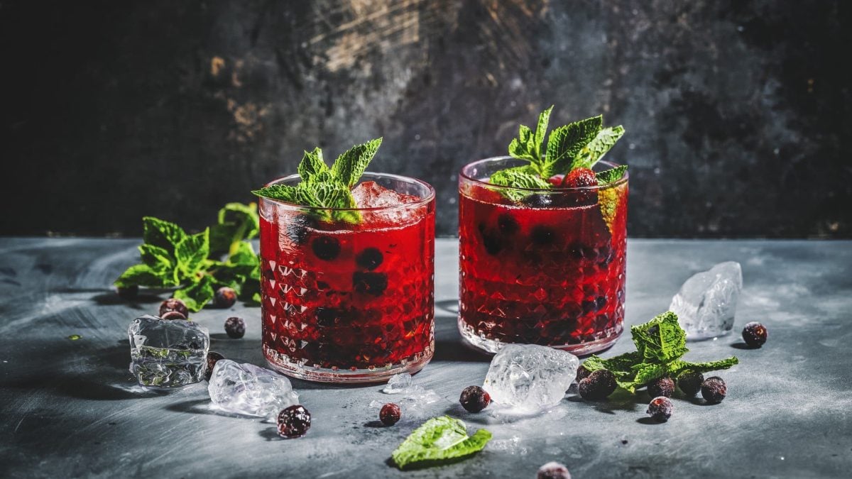 Zwei Gläser mit Blaubeer-Mojito und Minze garniert auf grauem Tisch mit Eiswürfeln.
