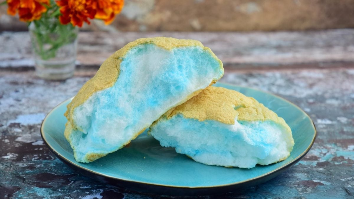 Ein blau-gelbes Brötchen auf einem Holztisch mit orangenen Blumen drauf.
