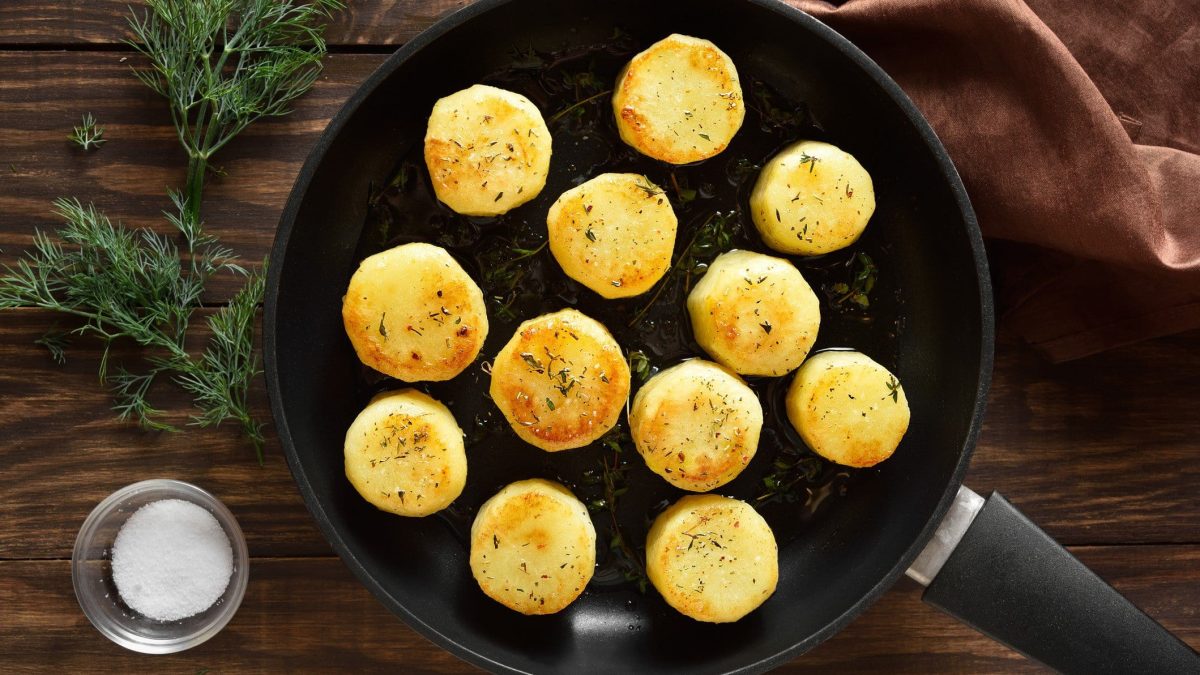 Fondant-Kartoffeln in einer Pfanne. Daneben liegt Rosmarin, eine Schale mit Salz und ein Küchentuch.