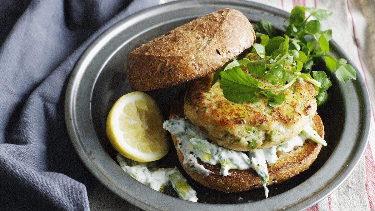 Saftiger Forellen-Burger-Patty auf einem klassischen Brötchen mit Tzaziki, garniert mit wildem Salat.