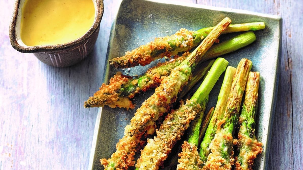 Frittierter grüner Spargel mit japanischer Sauce hollandaise, die in einem Kännchen daneben steht. Draufsicht.