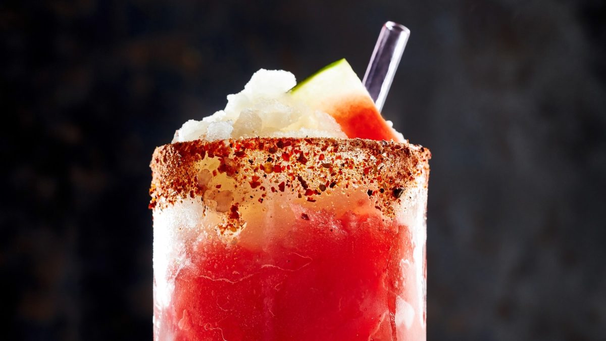 Ein Glas Frozen Melon-Margarita mit Crushed Ice, einer Melonenscheibe, einem Glashalm und gewürztem Rand.