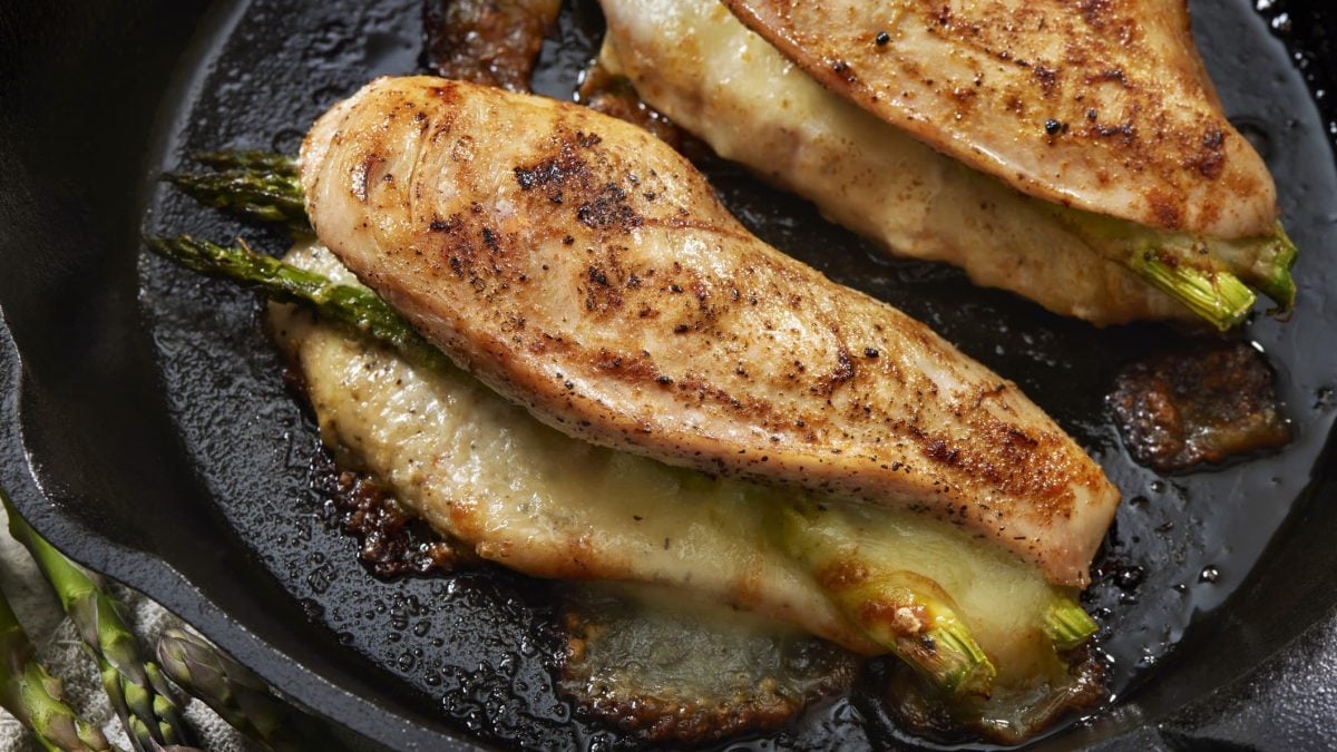 Gefüllte Hähnchenbrust mit Spargel und Provolone und einer gusseisernen Pfanne. Daneben weitere Spargelstangen.