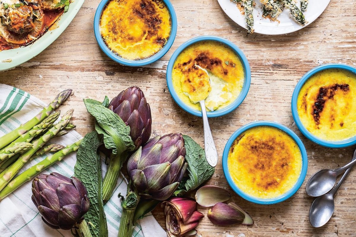 4 Schälchen Crème Brûlée mit grünem Spargel in der Draufsicht, drumherum andere Gerichte und frisches Gemüse wie Artischocken.
