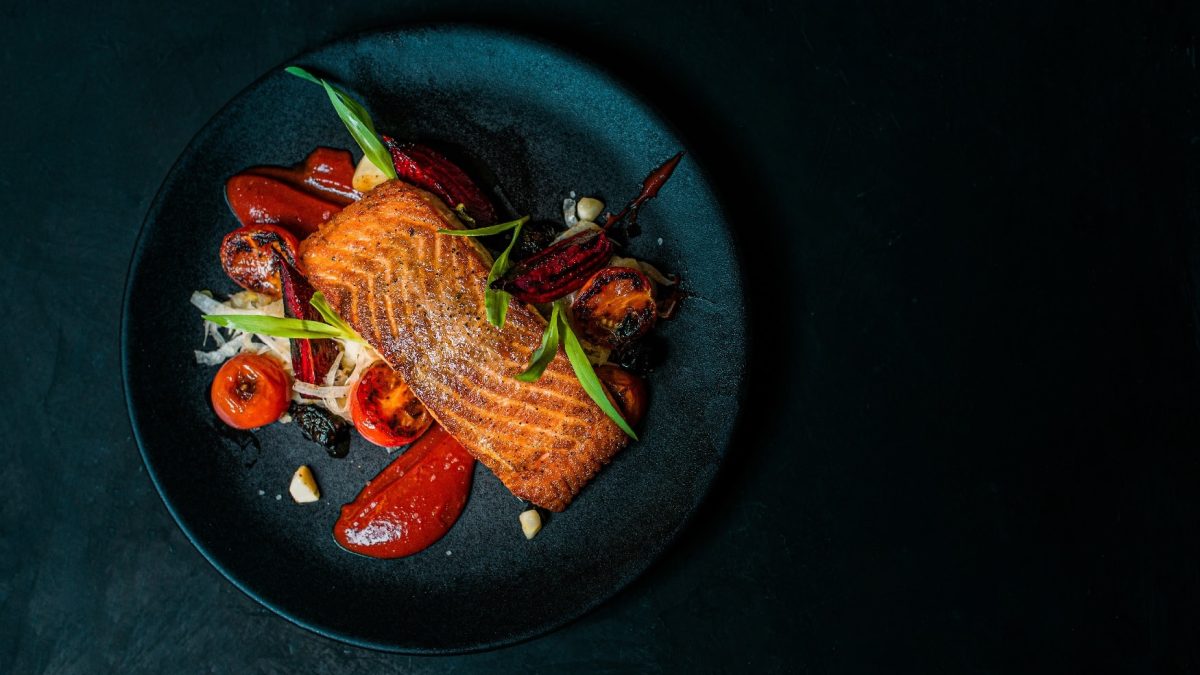 Draufsicht auf einen blauen Teller mit Lachs auf Fenchelsalat. Garniert mit roter Bete und Kirschtomaten.