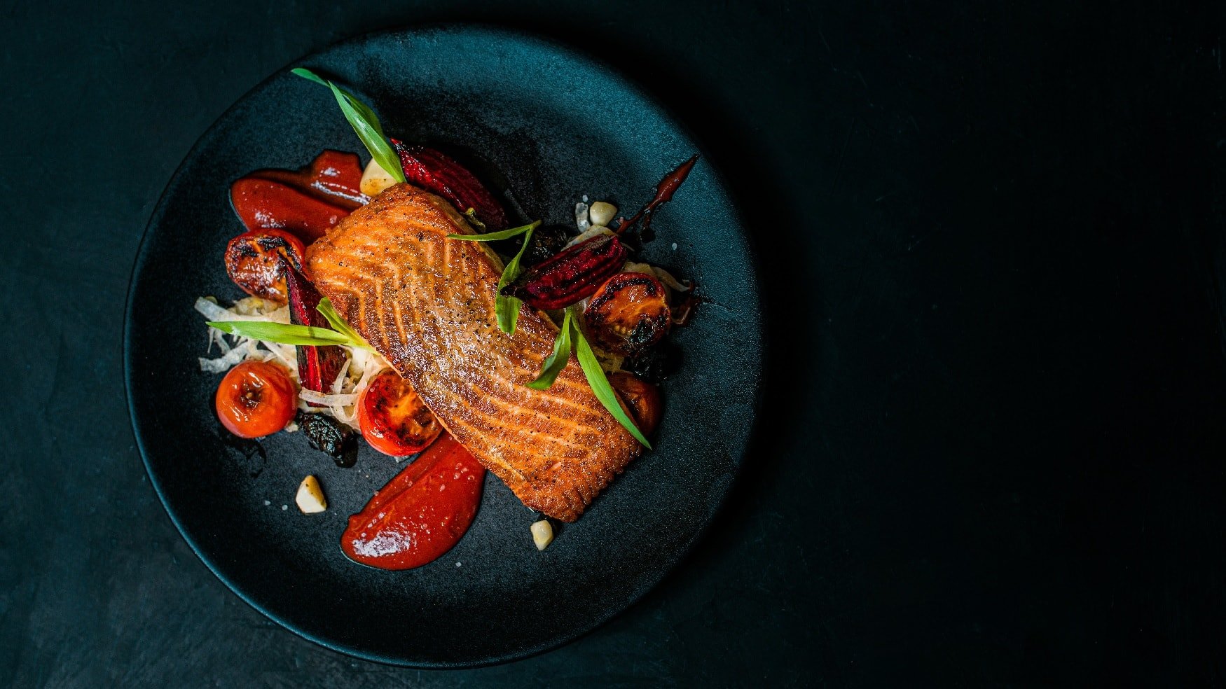 Draufsicht auf einen blauen Teller mit Lachs auf Fenchelsalat. Garniert mit roter Bete und Kirschtomaten.