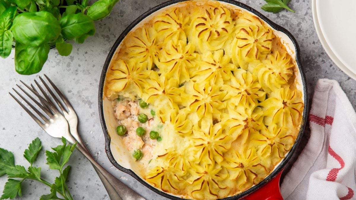 Lachs-Pie mit Erbsen und Kartoffelpüree überbacken, serviert in einer runden Auflaufform, serviert auf einem hellen Tisch.