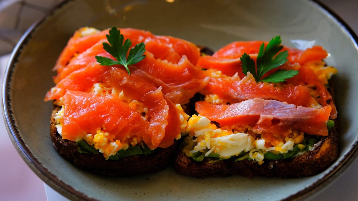 Zwei Scheiben Lachs Toast auf einem hellblauen Teller und hellem Untergrund.