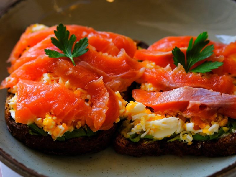 Zwei Scheiben Lachs Toast auf einem hellblauen Teller und hellem Untergrund.
