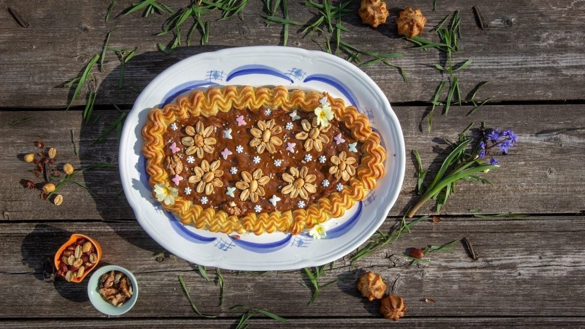 Klassischer polnischer Mazurek-Kuchen, bestehend aus Mürbeteig, einem gespritzen Rand, Marmelade, und feinen Dekor aus Nüssen und weiteren Zuckereien auf einem hölzernen Tisch.