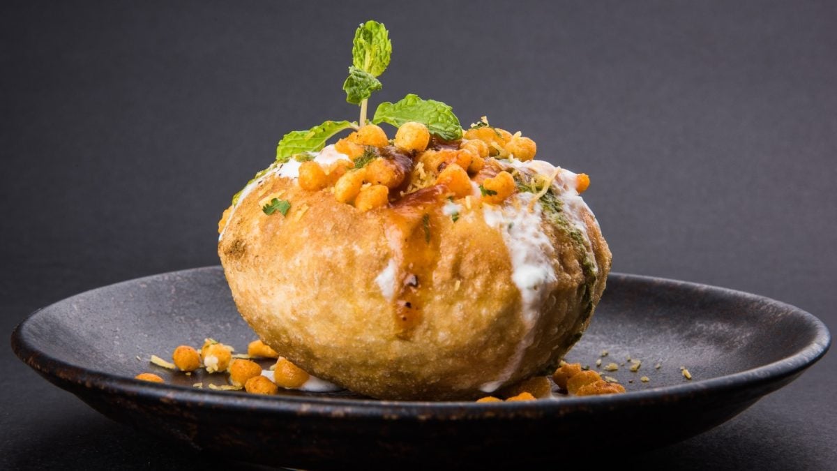 Ein Pani Puri Bällchen auf einem schwarzen Teller und schwarzem Hintergrund.