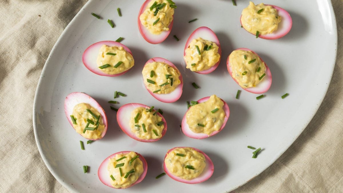 Pink deviled Eggs auf einem weißen Teller. Der Teller steht auf einem beigen Leinentuch.