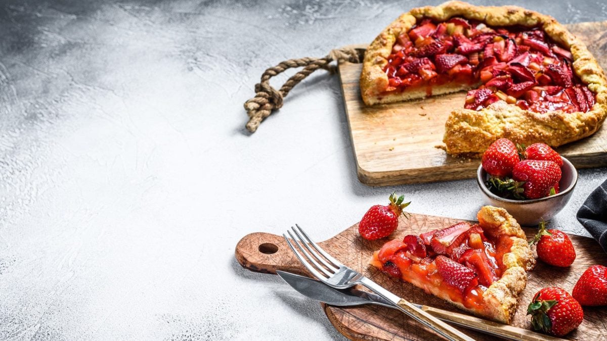 Erdbeer-Rhabarber-Galette-Tarte auf einem Holzschneidebrett und grauem Untergrund.