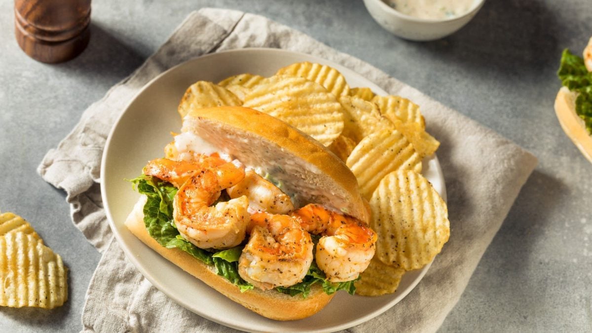 Cajun Shrimp Po Boy Shrimp po'boy Sandwich mit Chips auf Teller und weißem Leinentuch auf grauem Tisch. Chips, Pfeffermühle und Schale mit Remoulade auf dem Tisch. Aufnahme aus der Vogelperspektive.
